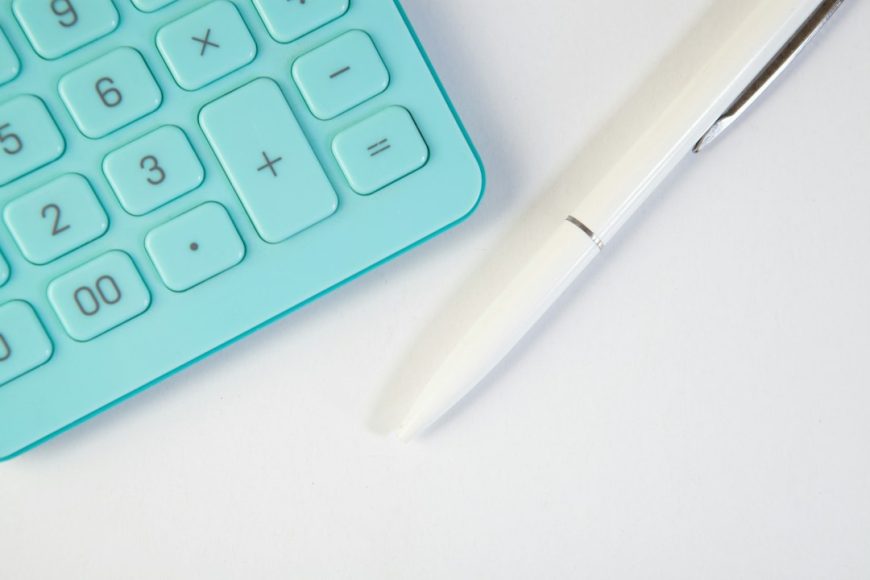 Calculator and pen arranged neatly on a white desk for small business marketing budget planning
